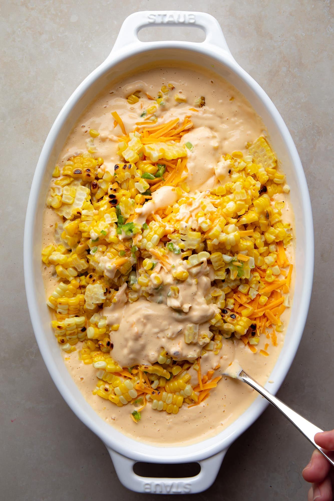 Usando uma colher para combinar os ingredientes para molho de milho vegano mexicano com um molho de caju cremoso em uma assadeira.